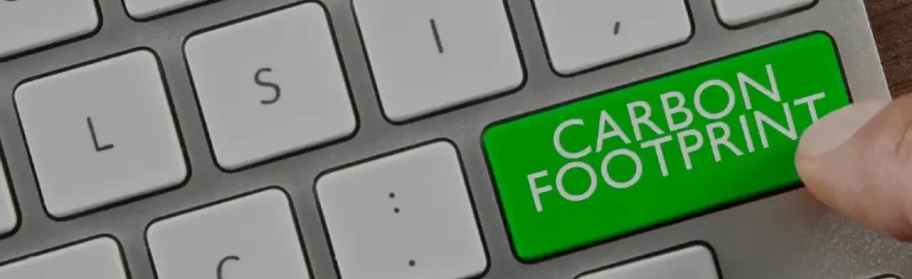 Dedo pulsando una tecla verde con el texto «Carbon footprint» en un teclado