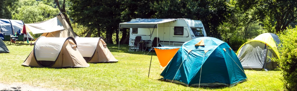 Camping con tiendas de campaña y una caravana sobre césped entre árboles