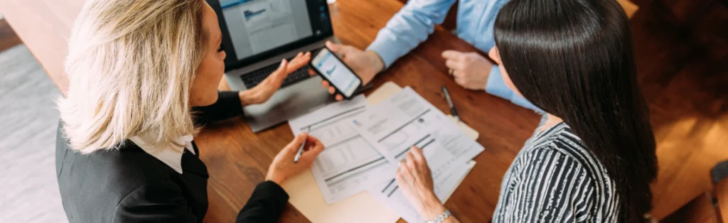 Tres profesionales revisan documentos financieros y un móvil sobre una mesa de trabajo